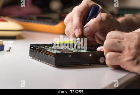 electronic engineer repairs computer hard drive. technologist with a screwdriver disassembles hdd Stock Photo