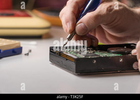 electronic engineer repairs computer hard drive. technologist with a screwdriver disassembles hdd Stock Photo