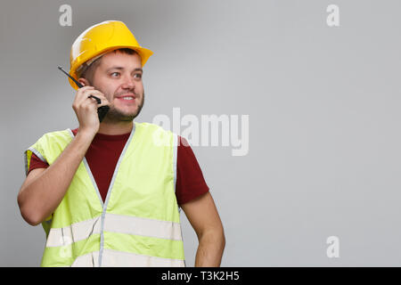 Image of cheerful builder in yellow helmet talking on radio in studio. Stock Photo