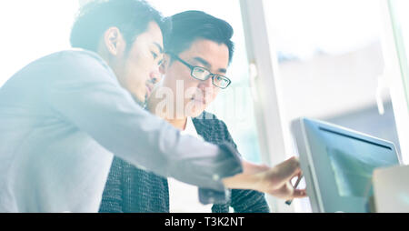 two young asian corporate executives working together using desktop computer.