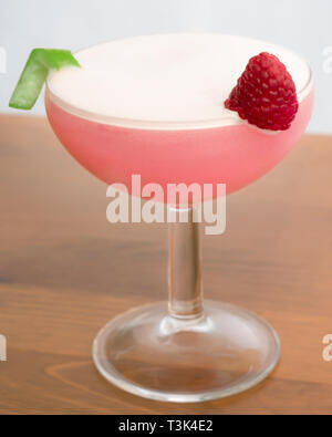 A Clover Club Cocktail in a coupe glass garnished with a raspberry and a lime twist Stock Photo