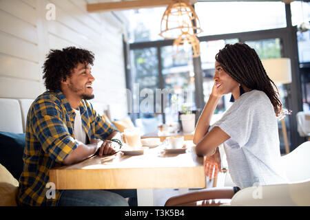 Smiling young african couple sitting at a table at a cafe drinking coffee and talking together Stock Photo