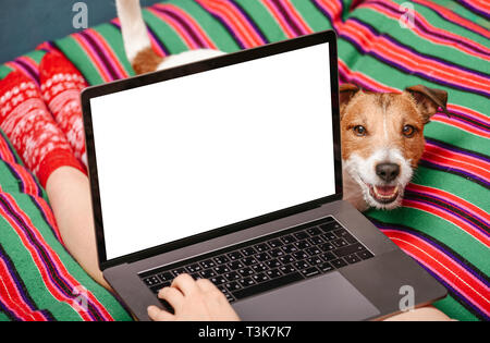 Mockup image of  young woman using laptop with blank white desktop screen and dog looking at owner Stock Photo