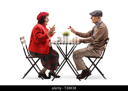 Full length profile shot of a senior man sitting at a cafe and giving a ring to a senior woman isolated on white background Stock Photo