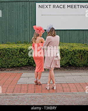 Two elegantly dressed woman standing in front of a next race meeting sign Stock Photo