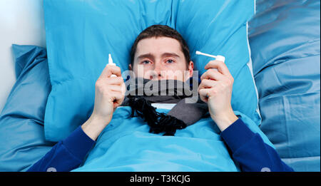 Photo of sick man with sprays in hands lying in bed Stock Photo