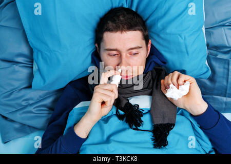 Sick brunet man using nasal spray while lying in bed Stock Photo