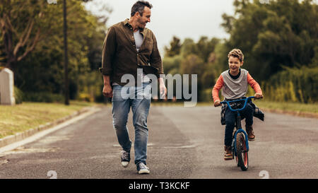Boy riding a bicycle while his father walks along. Kid learning to ride a bicycle with his father. Stock Photo