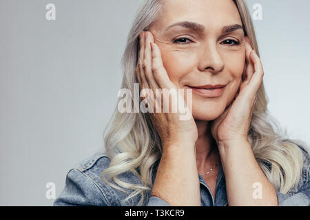 Beautiful elderly woman touching her soft skin. Woman with beautiful skin against grey background. Stock Photo