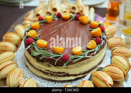 Sweet chocolate cake with cream, fresh oranges and raspberries with cookies around Stock Photo