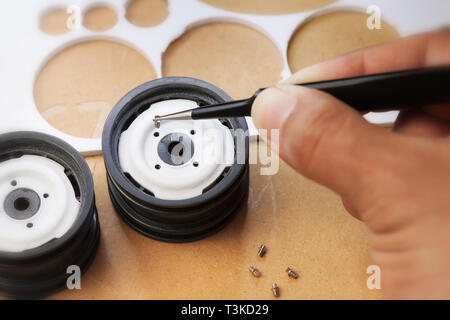 Craftsman putting a tiny screw into a scale wheel with precision for miniature handmade toys. Stock Photo