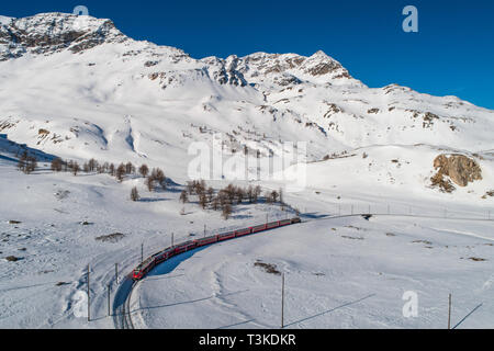 Red train of Bernina in winter season, aerial view. Bernina Express - UNESCO Stock Photo