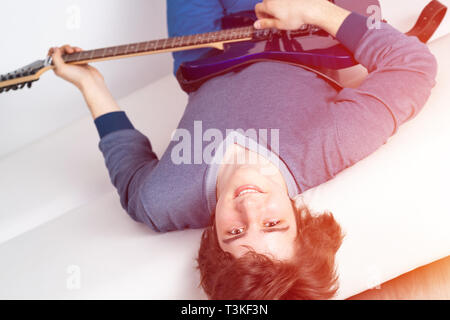 Happy young man lying back on sofa with guitar Stock Photo