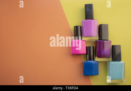 Bottles of nail polish. A group of bright nail polishes on a colored, yellow background. With empty space on the left. View from above Stock Photo