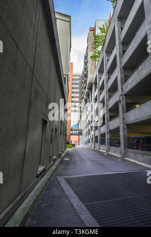 A deserted lane way with a parking garage on the right side. Garbage bins and an elevated walkway are in the distance. Stock Photo