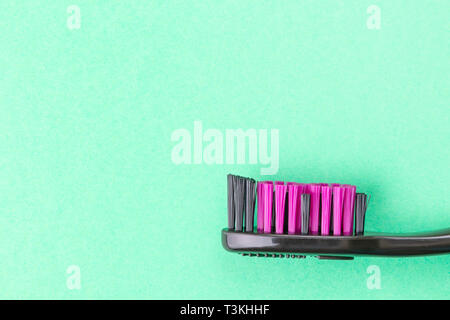Black and pink toothbrush closeup on a green background. The bright image is suitable as a background for the topic of dentistry and dental care. Stock Photo