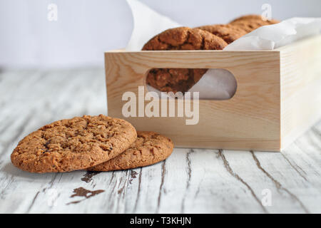 Box of fresh homemade oatmeal cookies on a white table against a white background.. Selective focus on two lying on table. Stock Photo