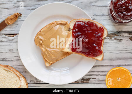 Top view of open face homemade peanut butter and strawberry Jelly sandwich on oat bread, over a white rustic wooden table / background. Served with fr Stock Photo