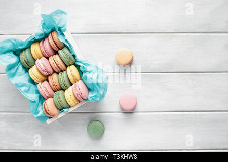 Assortment of fresh french macarons packaged in a pretty white wooden box with blue tissue on a white rustic table. Image shot from above with room fo Stock Photo