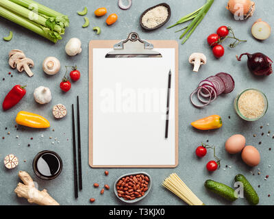 Asian ingredients and clipboard with white paper sheet. Various of Chinese cooking ingredients and chopsticks on gray stone background. Asian food concept. Copy space for text. Top view or flat lay.