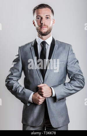 bearded young business man in a silver gray shiny elegant suit with black collar white shirt and black tie Stock Photo