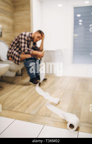 Sad man with hangover sitting on toilet