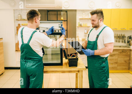 Technicians in uniform repair refrigerator at home Stock Photo