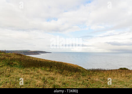 Runswick Bay from Kettleness with green grass, calm sea and blue and cloudy sky Stock Photo