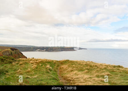 Runswick Bay from Kettleness with green grass, calm sea and blue and cloudy sky Stock Photo