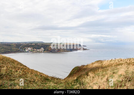 Runswick Bay from Kettleness with green grass, calm sea and a blue and cloudy sky Stock Photo