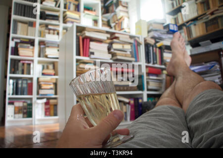 Adult man enjoying his leisure time, drinking wine and relaxing looking at bookshelves. Selective focus, space for text. Stock Photo