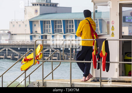 RNLI Lifeguard on duty at Lifeguards kiosk hut with Bournemouth Pier in the background at Bournemouth beach, Bournemouth, Dorset UK in April Stock Photo