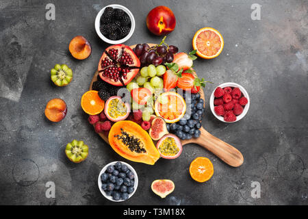 Delicious fruit platter pomegranate papaya oranges passion fruits berries on wooden board on dark concrete background, selective focus Stock Photo