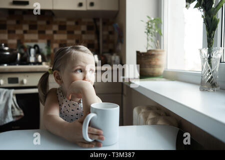 Little cute girl sitting at the table in the kitchen Stock Photo