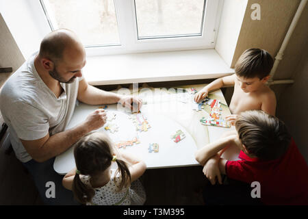 Father, daughter and sons play in the kitchen, they put together a puzzle