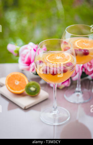 Orange vodka cocktail in elegant wine glass with kiwi, roses and raspberries Stock Photo