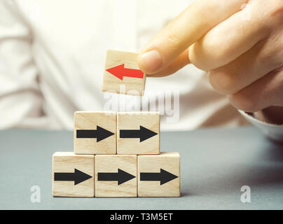 A man holds a wooden block with red arrow facing the opposite direction black arrows. Individual opinion. Stand out from the crowd. Uniqueness. Diverg Stock Photo