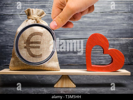Euro money bag and red wooden heart on the scales. Money versus love concept. Passion versus profit. Family or career choice. Family psychology. Mind  Stock Photo