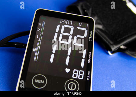 Close up of digital monitor device with cuff showing high diastolic and systolic blood pressure. Blue background. Stock Photo