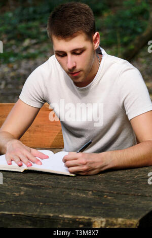 Guy and student takes notes in notebook, learning and writes thoughts, writes the book, he is preparing his final exams doing homework and thinking. Stock Photo