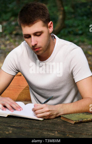 Guy and student takes notes in notebook, learning and writes thoughts, writes the book, he is preparing his final exams doing homework and thinking. Stock Photo