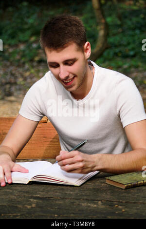 Guy and student takes notes in notebook, learning and writes thoughts, writes the book, he is preparing his final exams doing homework and thinking. Stock Photo
