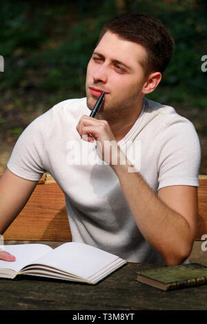 Guy and student takes notes in notebook, learning and writes thoughts, writes the book, he is preparing his final exams doing homework and thinking. Stock Photo