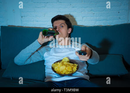 Lifestyle portrait of young man sitting on the coach watching switching channels with remote control looking for sports or movie to watch at home late Stock Photo