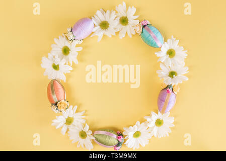 Wreath of Easter eggs and white daisies on solid pastel yellow background Stock Photo