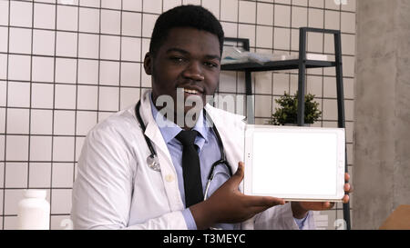 Handsome serious African doctor presenting product on tablet screen. White Display. Stock Photo