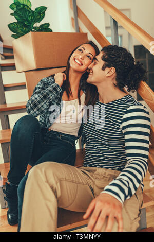 The young couple is moving into a new house. They are sitting on stairs and resting after bringing boxes with things to their new home. Stock Photo