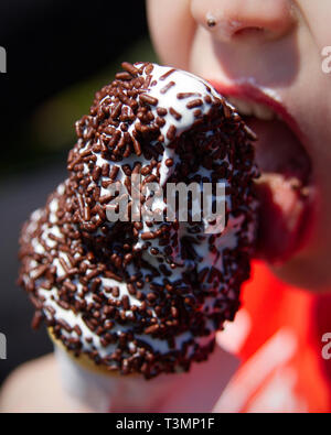 Close up of a young boy licking a vanilla ice cream cone covered in chocolate sprinkles. Stock Photo