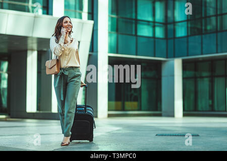 A young woman is going on a business trip through the office district against urban city background and carried a suitcase with her. Stock Photo