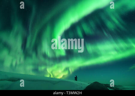 Aurora and silhouette of alone standing man on the hill. Lofoten islands, Norway. Aurora borealis and photographer. Sky with stars and green polar lig Stock Photo